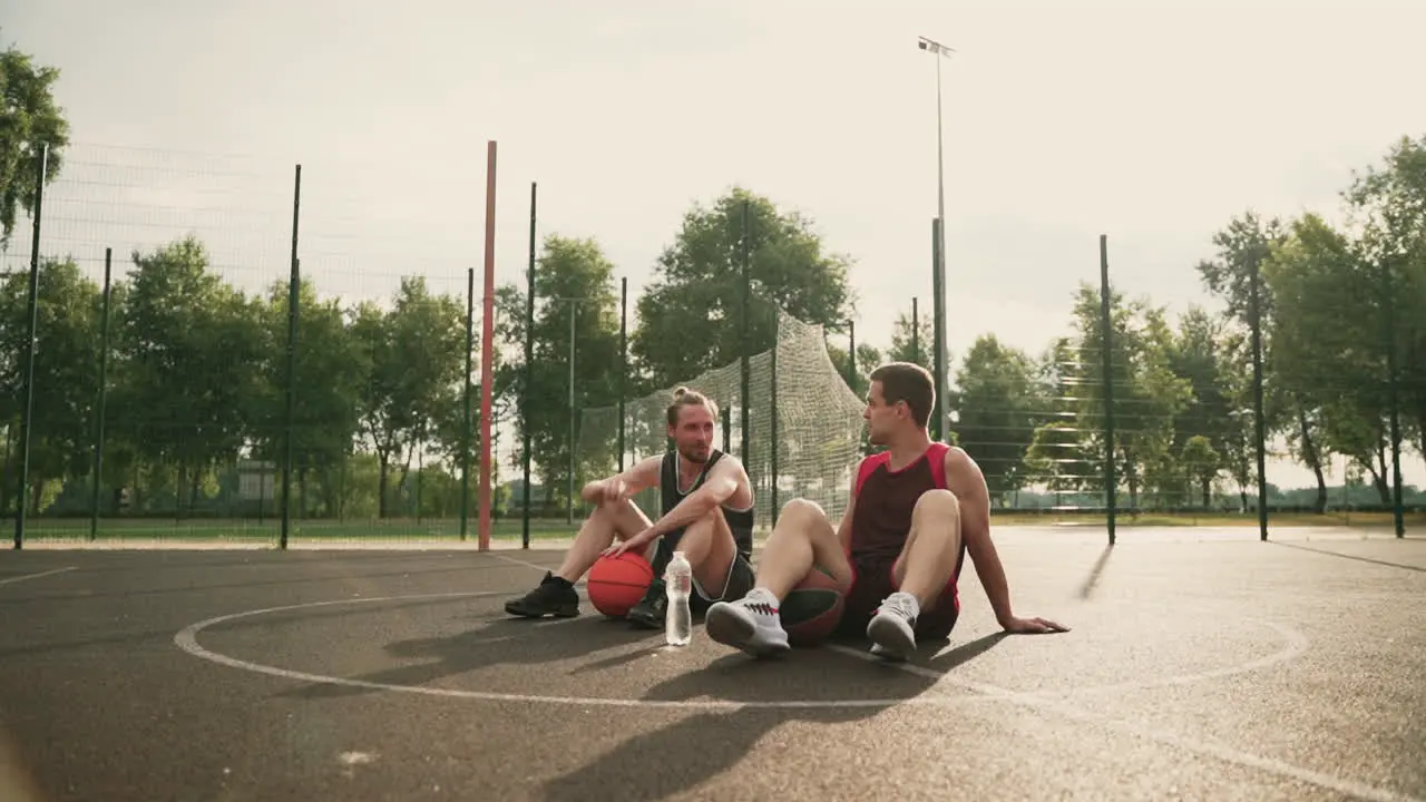 Zwei Glückliche Basketballspieler Sitzen Mitten Auf Einem Basketballplatz Im Freien Machen Eine Pause Und Unterhalten Sich über Ein Interessantes Thema