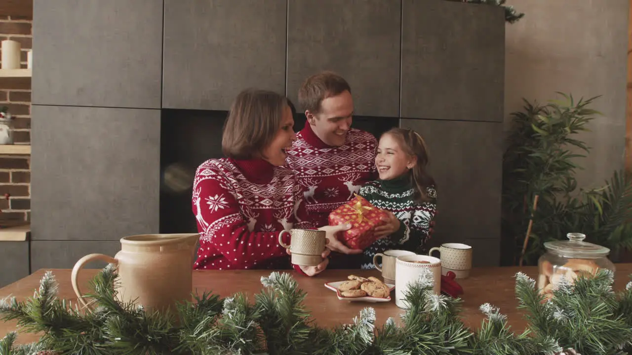 Amorosos Padres Dando Un Regalo Sorpresa A Su Pequeña Hija Mientras Desayunan Juntos Con Bebidas Calientes Y Galletas El Día De Navidad En Casa