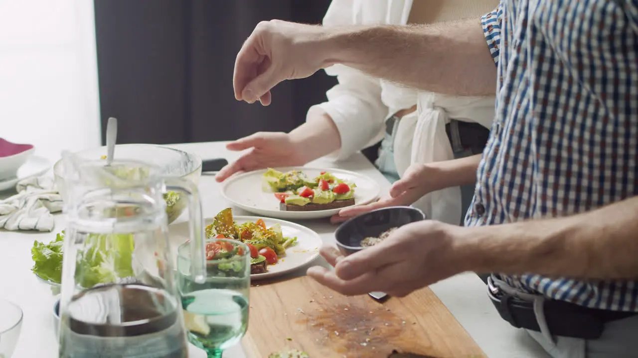 Primer Plano De Un Hombre Que Agrega Una Mezcla De Semillas A Una Deliciosa Ensalada En Su Plato Mientras Su Esposa Está De Pie Junto A él Con Su Plato