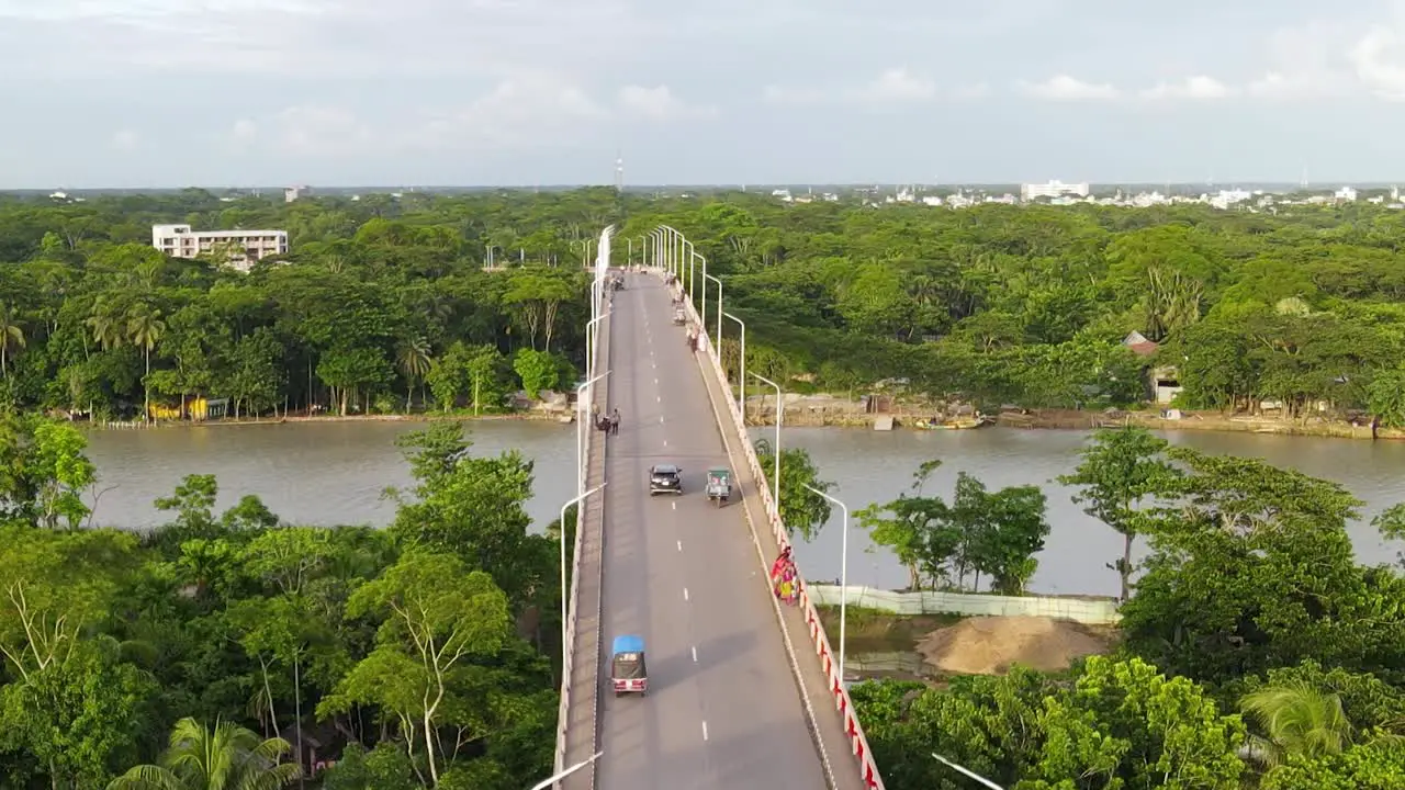 Aerial descending view of Viaduct bridge over River with Forested riverbank vehicles driving by Bangladesh