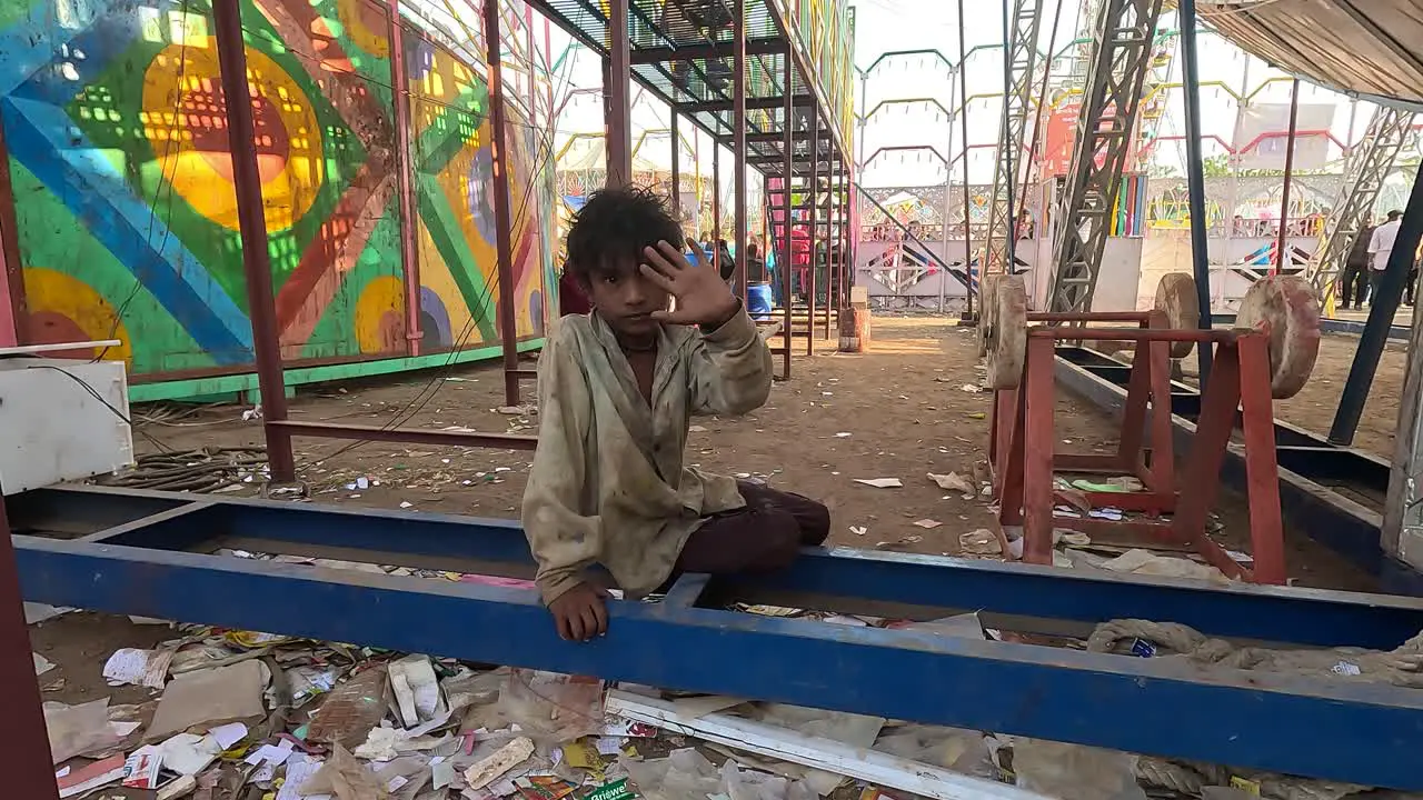 A slum kid is sitting under the amusement doing tata bye bye to the camera