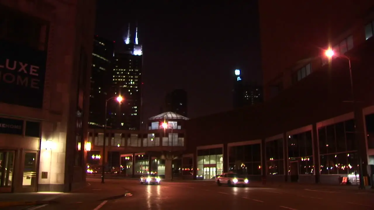 Nighttime Urban Scene With Taxis And Other Vehicles Traveling Across An Intersection With Chicago Landmark The Sears Tower In The Background