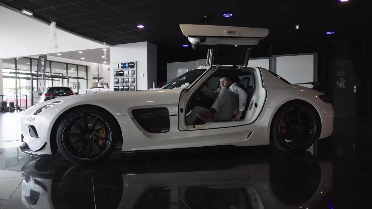 Slow motion shot of a prestigious man leaving a white Mercedes-Benz AMG GT in a showroom