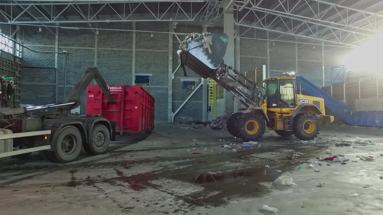 Excavator loading trash into container in recycling yard during sunny day slow motion