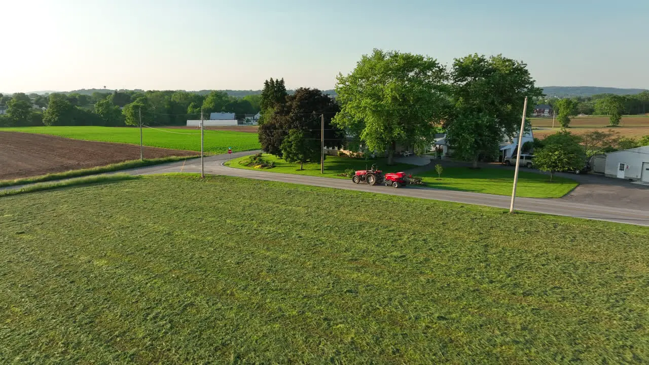 Aerial approach towards red tractor with baler attached