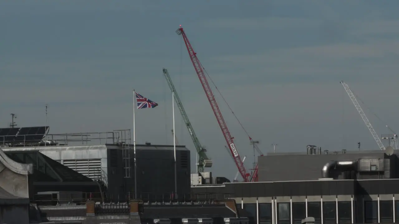 Rooftop View Of Construction Cranes Moving And Union Jack On Flagpole In London