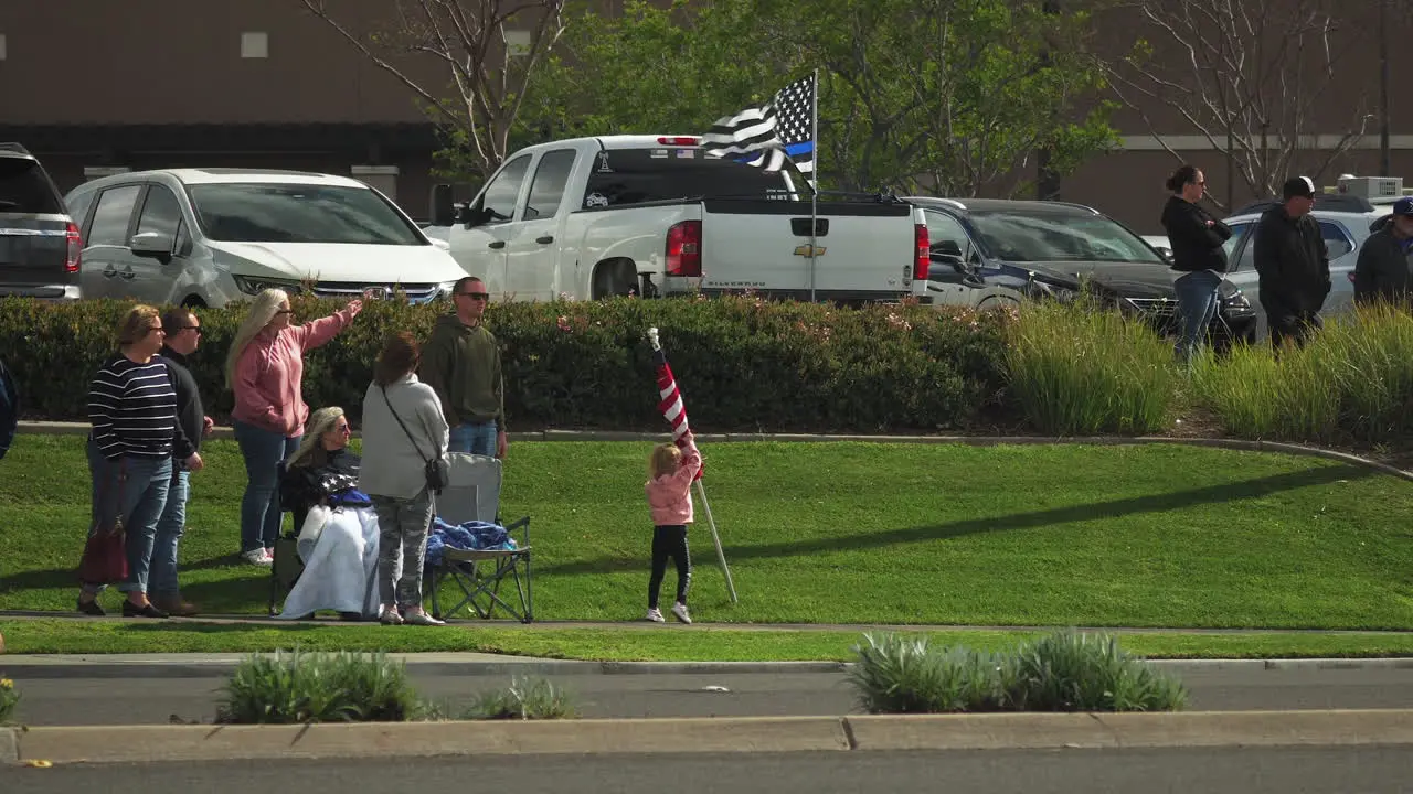 A family waves an American flag as a funeral procession drives by