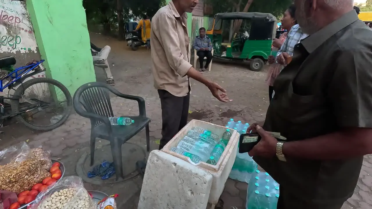 A shopkeeper is selling cold bottles of water on the street road and taking money from customers