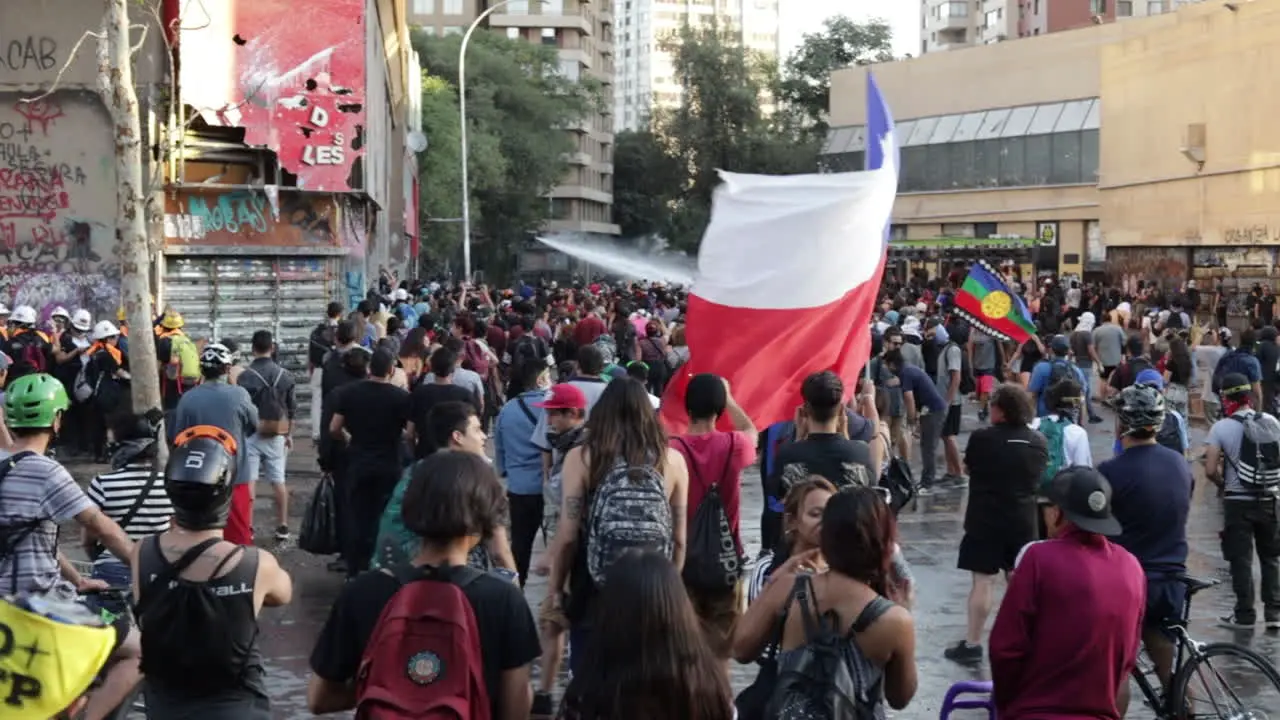 Man carries a large Chilean flag through the crowd of protesters in the streets of Santiago