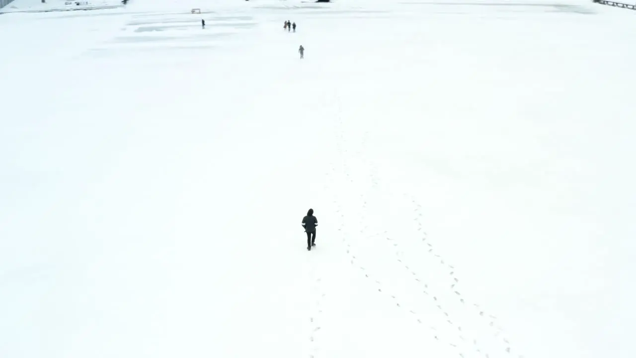 An aerial drone shot orbiting a person walking in the middle of a frozen lake in the winter