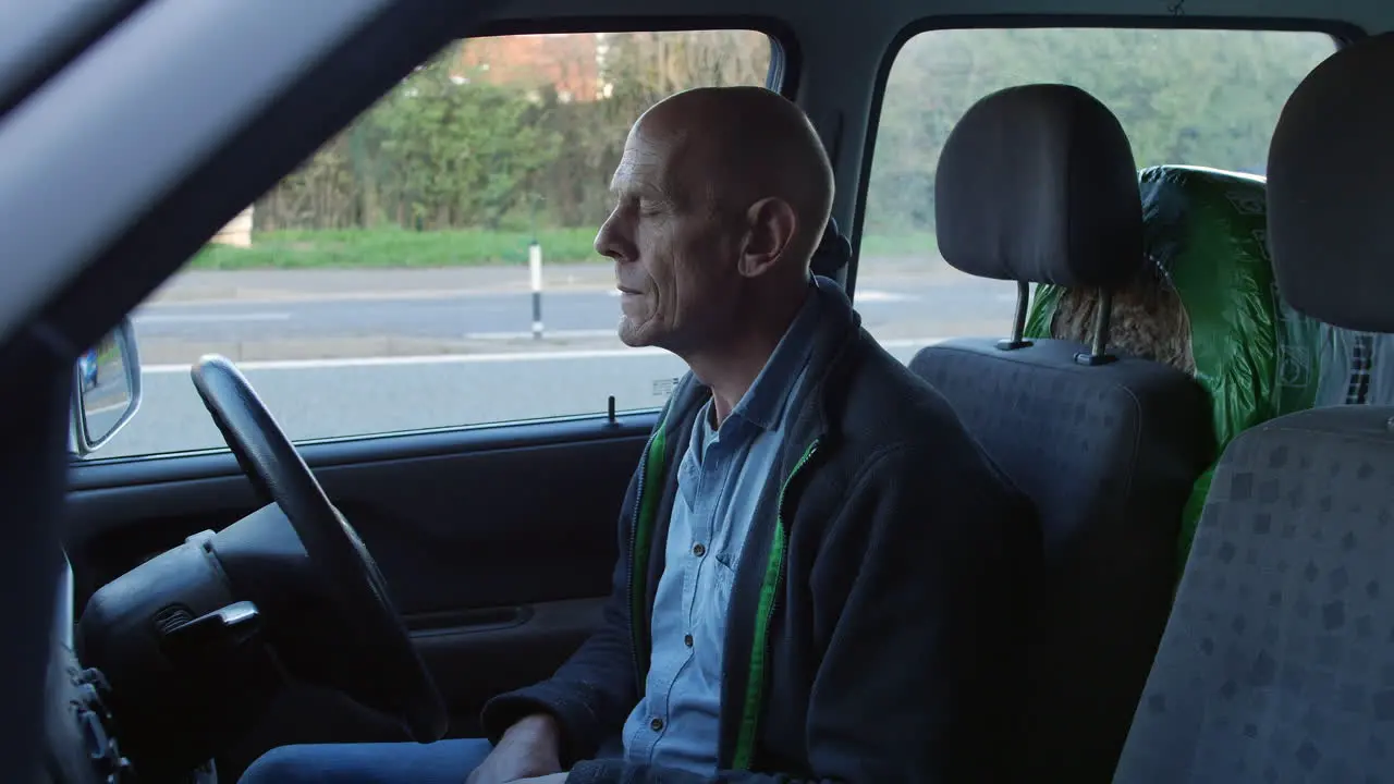 A mature man sitting hin his car bored and pensive as traffic passes on a busy road