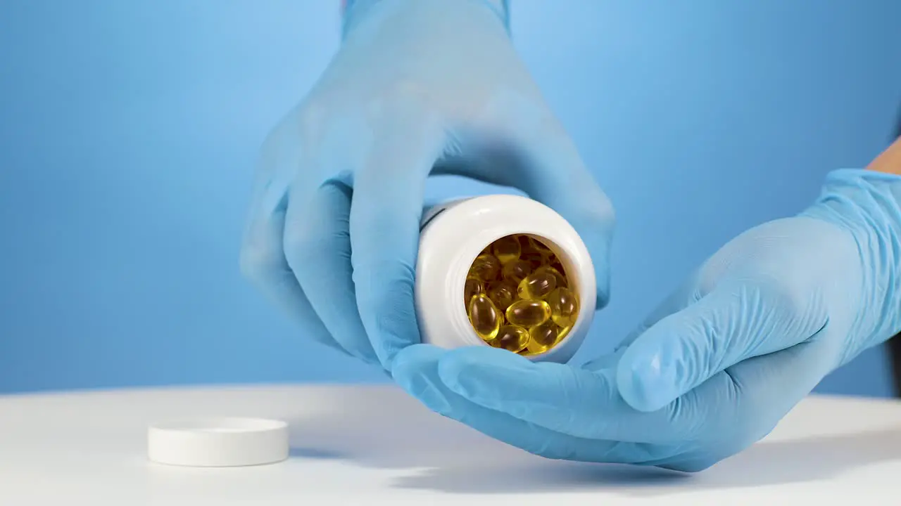 Pharmacy worker pours omega fish oil capsules in hand with blue glove slowmo