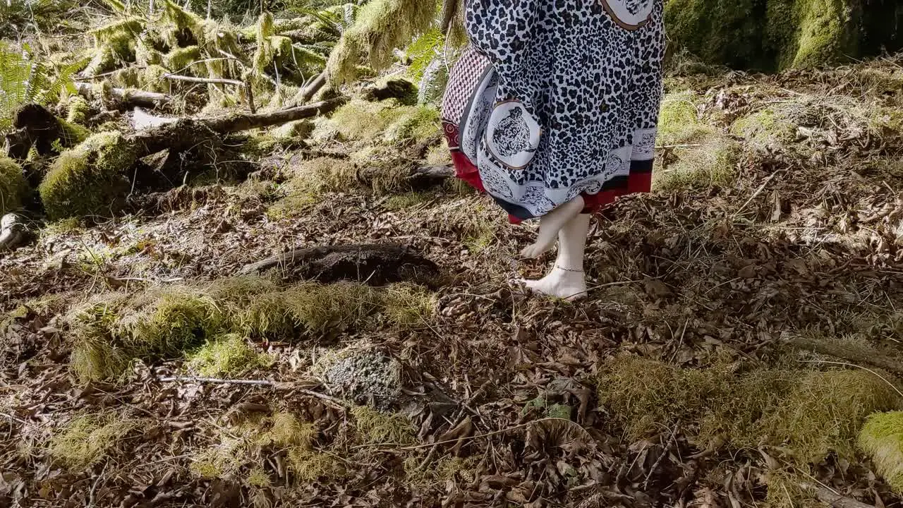 Woman shaman walking barefoot from right to left on moss covered rainforest ground while thanking her ancestors for her abundance