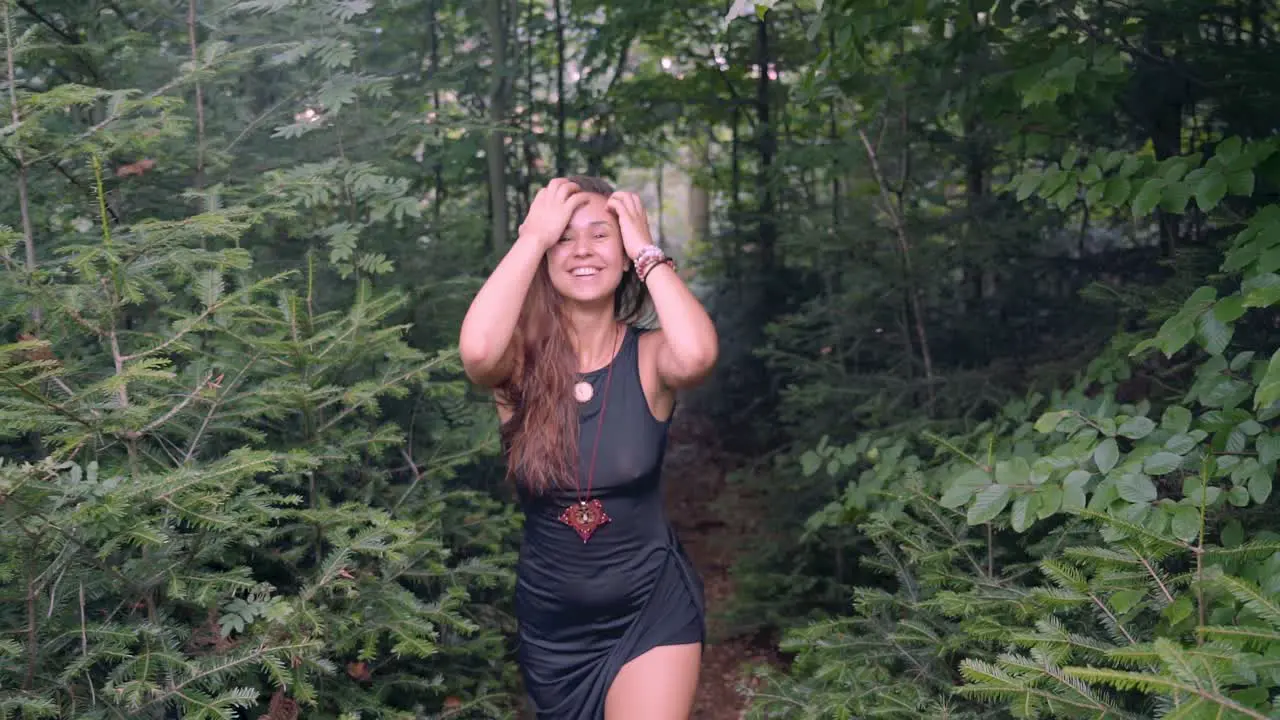 Slow motion follow up shot from front of young happy sexy and beautiful girl walking with a smiling face in the middle of dense forest