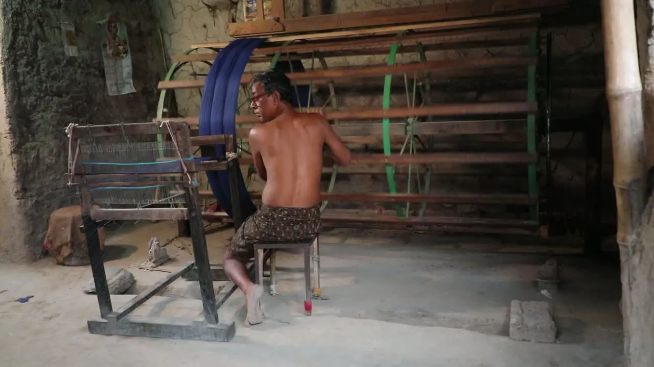 Rural worker spinning blue cotton threads in machine in textile factory cloth manufacturing industry