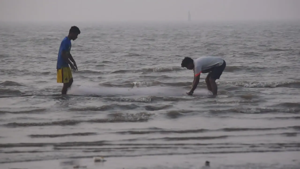 Two Indian Fisherman preparing and cleaning fishing net near a beach shore before going for fishing in sea video background in prores 422 HQ