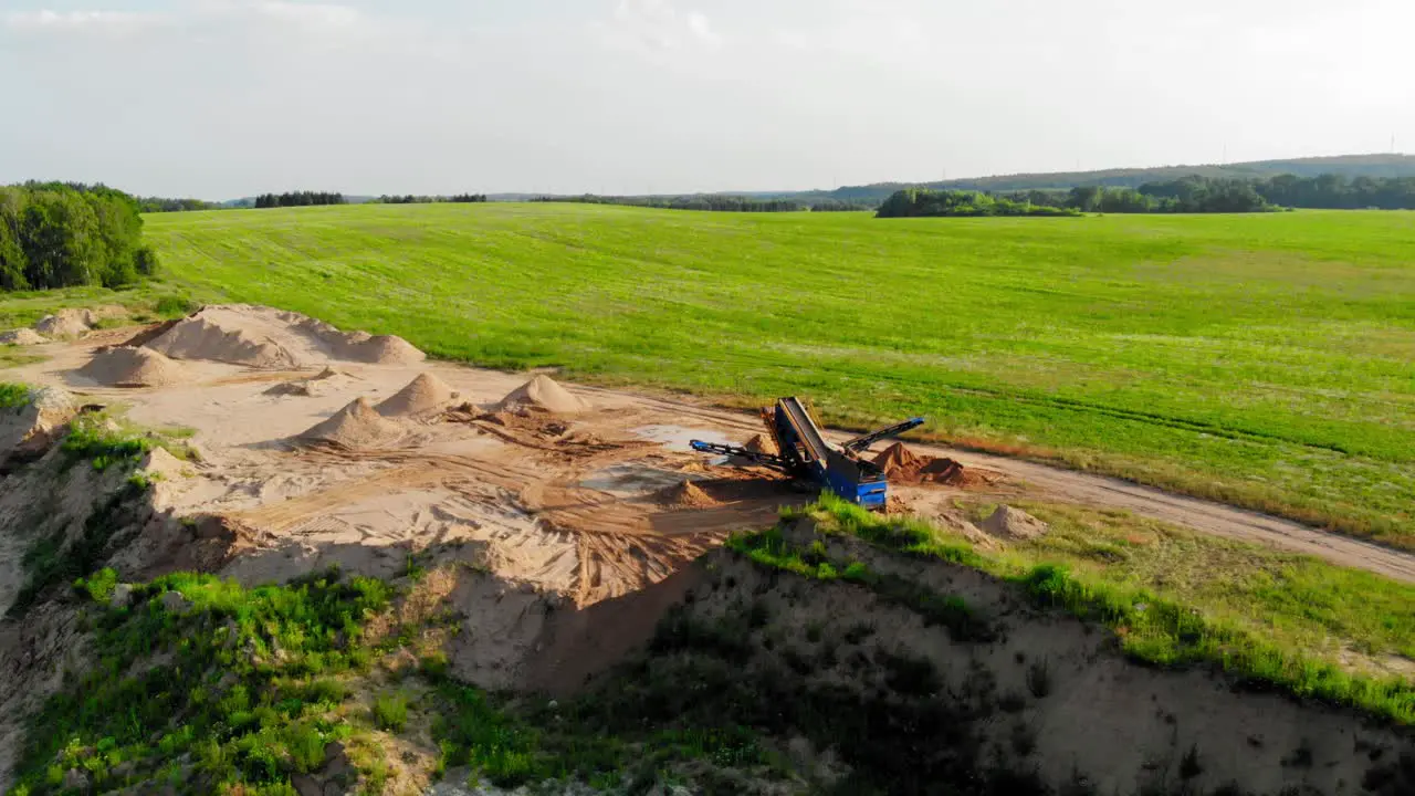 Aerial boom shot from a drone of quarry heavy machinery and green meadow in pomeranian district in Poland showing contrast between nature and industry