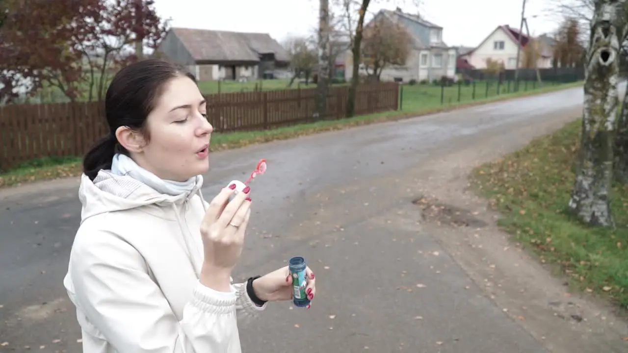 Side shot of young female blowing soap bubble outdoor wind blows away on the street in the autumn