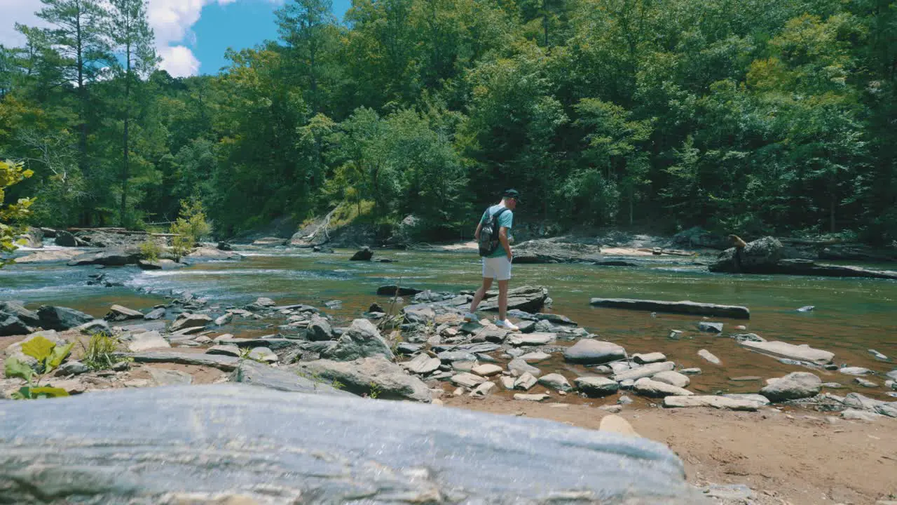 A reveal of a man walking alongside a steady flowing river gazing at its beauty