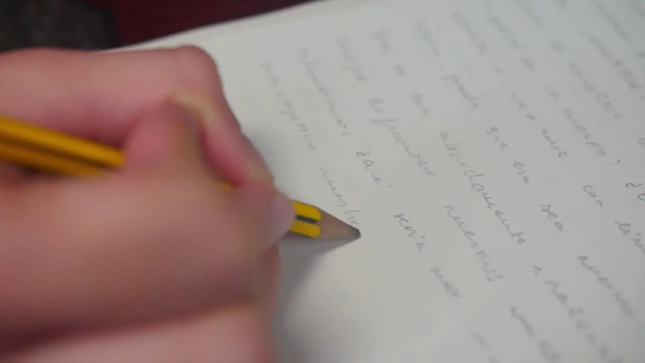 Close-up of hands writing words in Spanish with a pencil in slow motion on a white sheet of paper