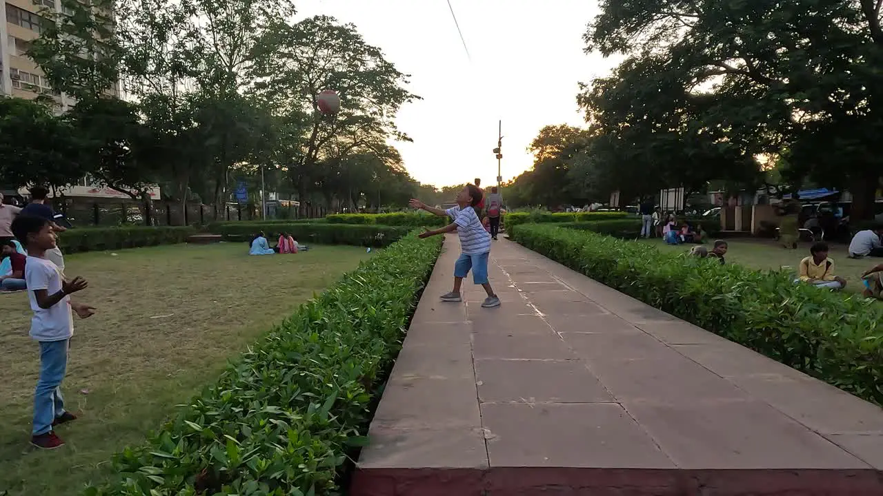 Young children playing volleyball and football on the walkway in a public park