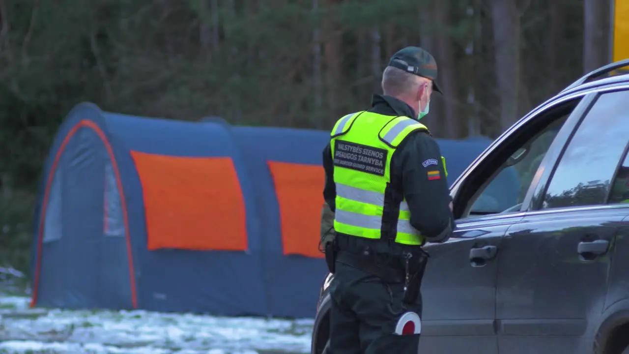 Lithuanian border guard officer stops passenger car at the Lithuania Latvia border during crisis measures in the fight against the novel coronavirus Covid-19 medium shot from a distance