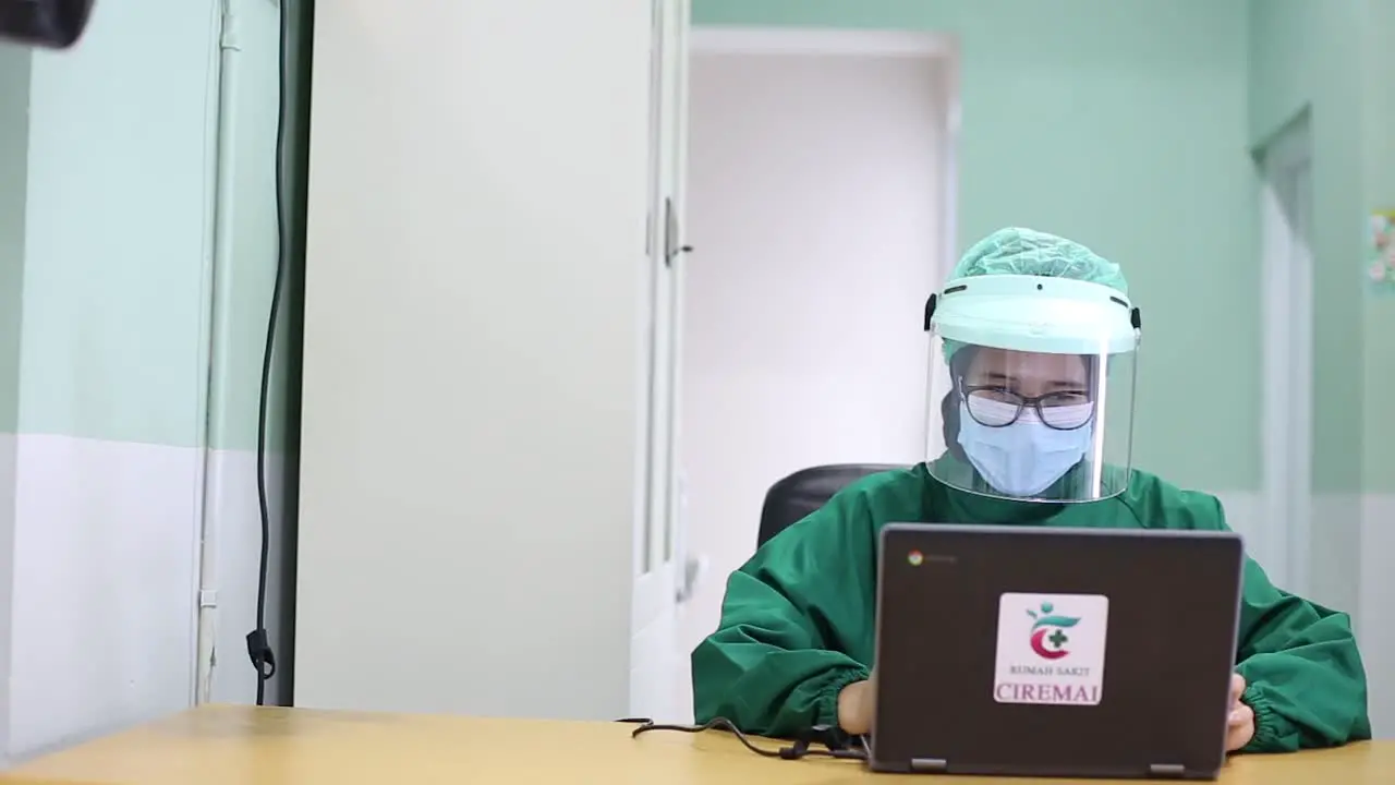 Young Asia lady doctor in blue medical uniform with hijab using computer laptop talking video conference call with patient at desk in health clinic or hospital