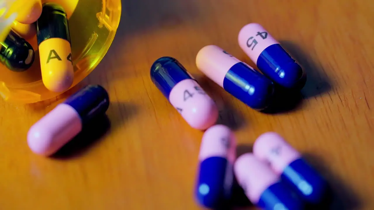 Prescription bottle filled with pink and blue pills spills in slow motion to scatter contents close to the camera's macro lens