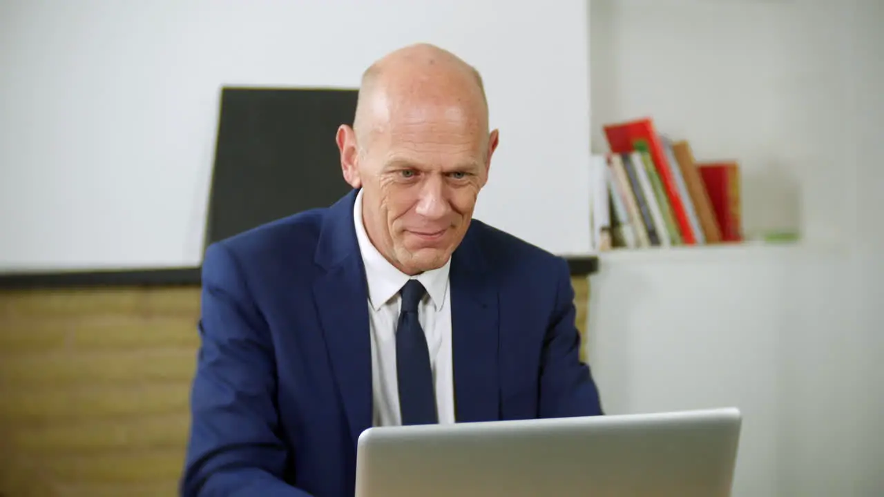 A happy mature businessman is working on his laptop in his home office