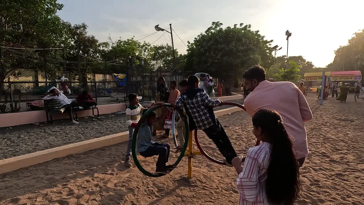 A father amuses his children by putting them on a rounding ride and turning them by hand