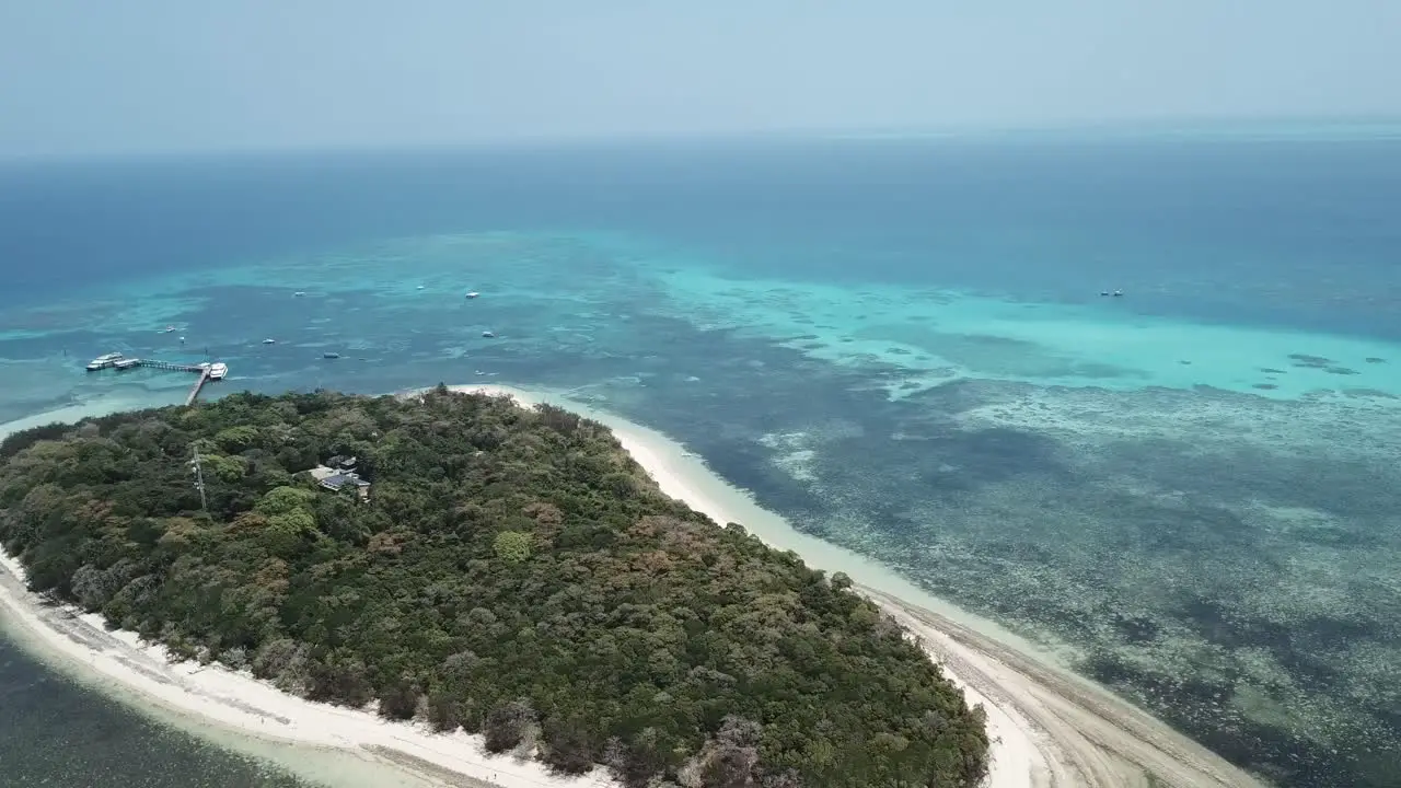 Drone aerial over small tropical forest island around a clear blue reef