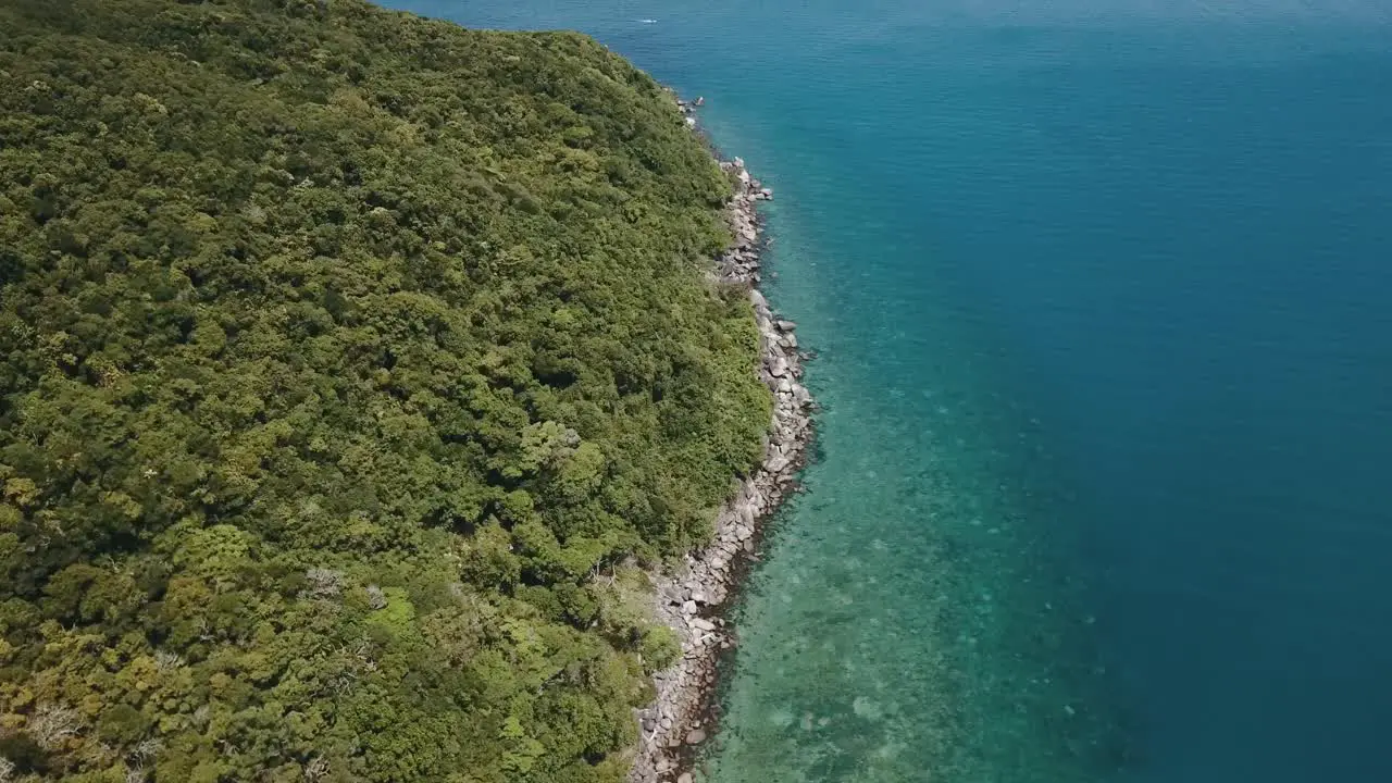 Drone aerial pans up to show a tropical island with clear blue water and sandy beaches on the Great Barrier Reef