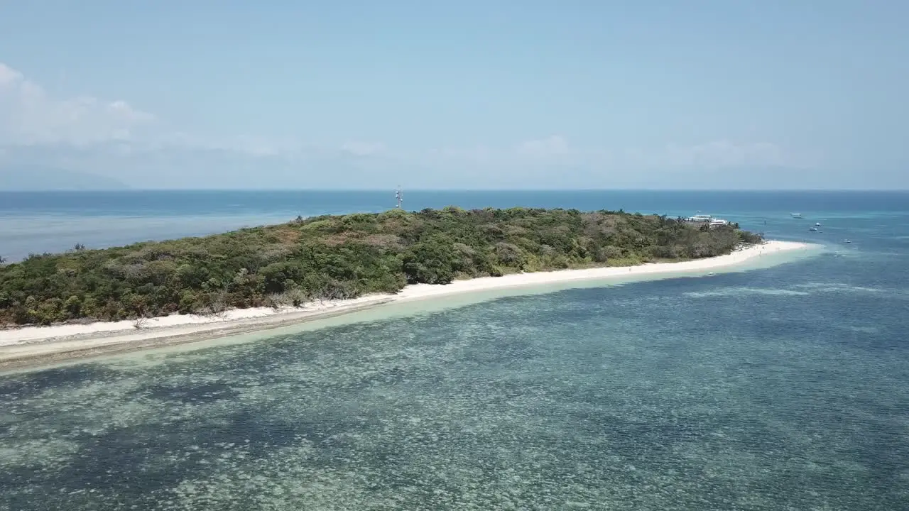 Drone aerial moving towards island that's tropical with white sandy beach and blue reef water