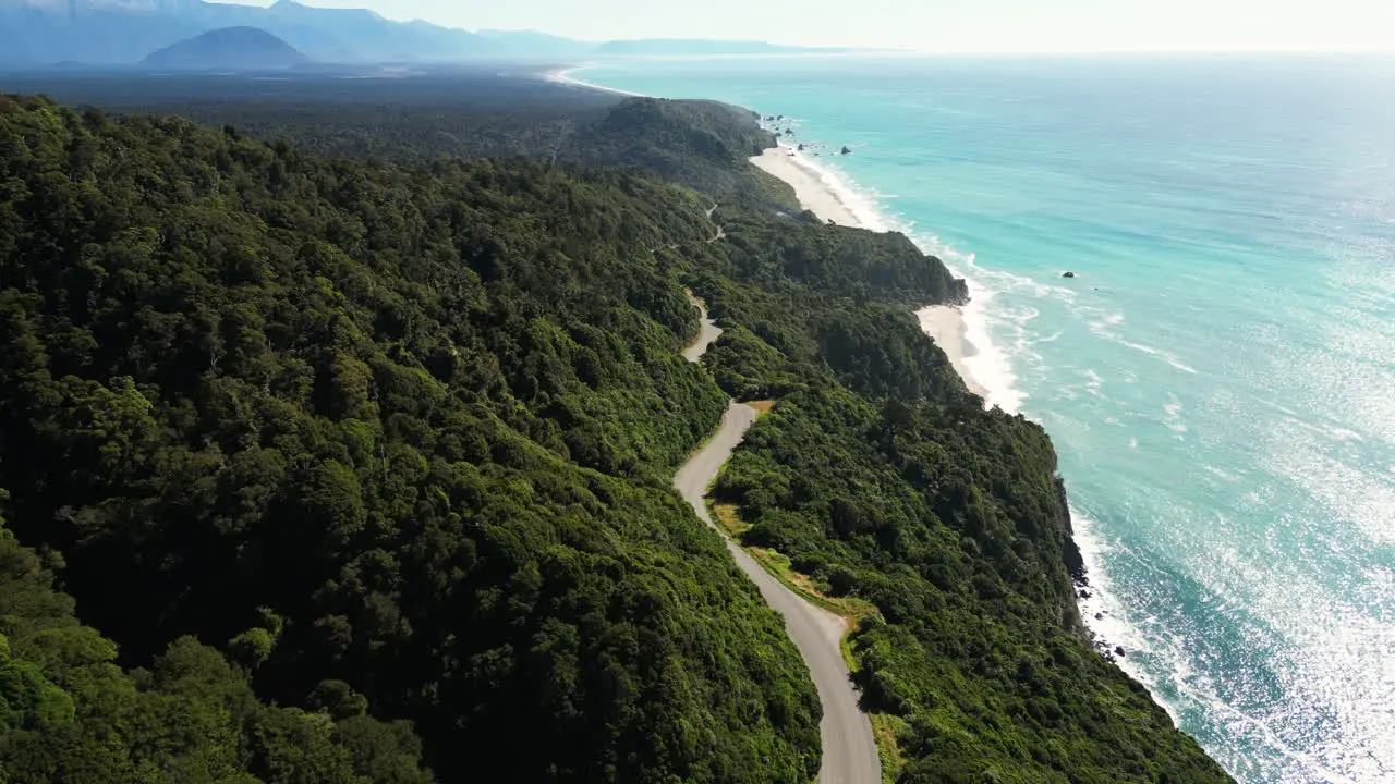 New Zealand aerial view of sunny weather in west coastline with asphalted road following the coastline of the blue ocean water in green lush forest