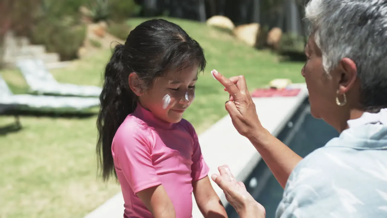 Biracial man applies sunscreen on a biracial girl's face outdoors