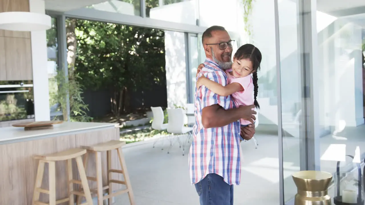 Biracial grandfather in a plaid shirt carries a young biracial granddaughter indoors