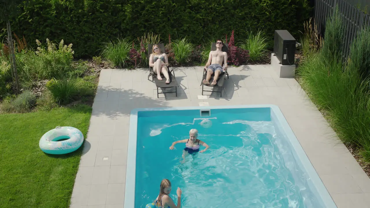 Senior woman is playing with her granddaughter in the pool her parents are sunbathing on sun loungers nearby Family holiday by the pool