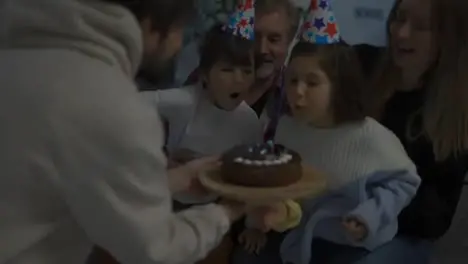 Little brother and sister blows out the candles on cake together in a circle of happy family