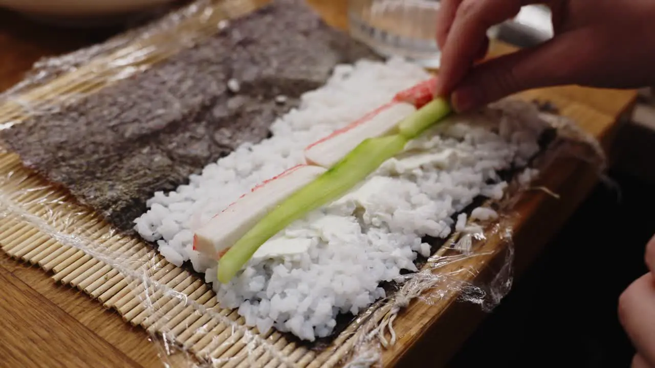 Person Placing Cucumber Next To Crab On Rice In Sushi Roll Homemade Preparation