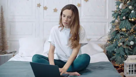 Concentrated female sitting with notebook on sofa in new year decorated house