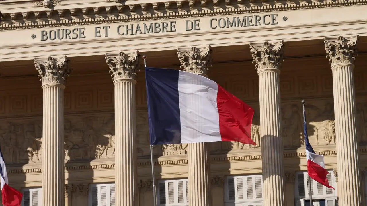 French flag moving in the wind in front of a building inspired by antique Greece columns with its shadow on the wall of the business center