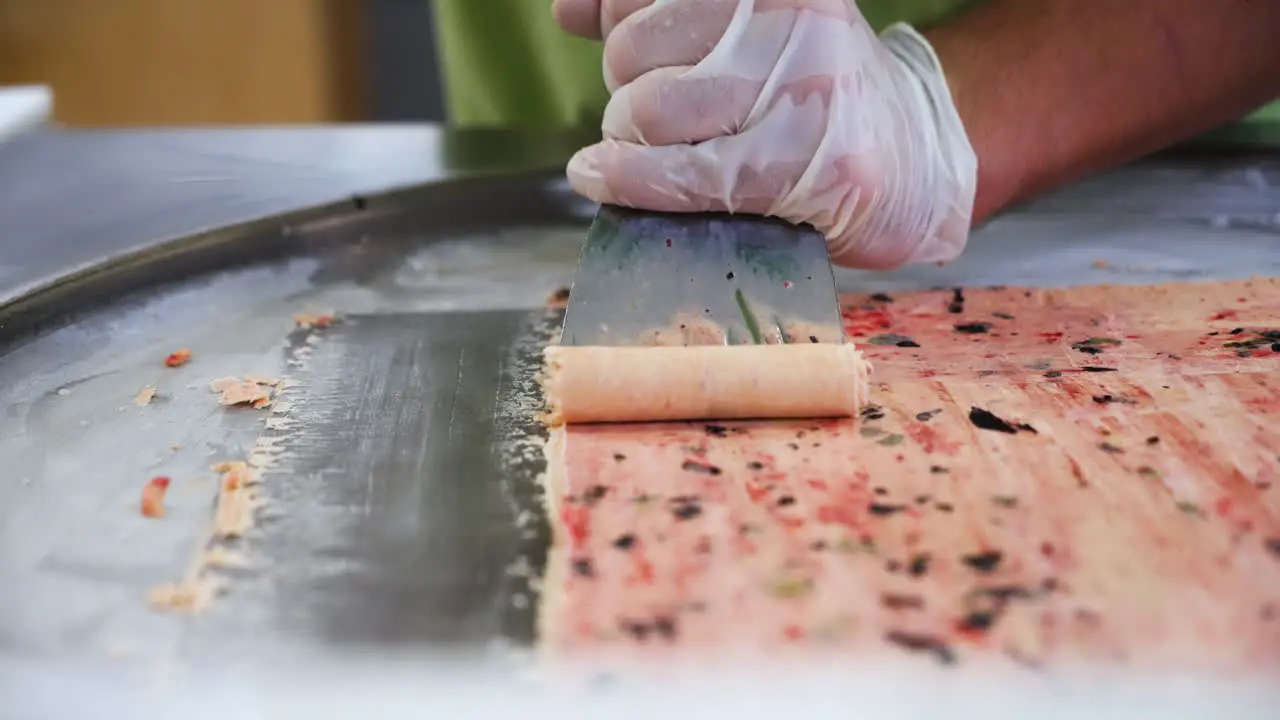 Worker carefully pushes up rolls of Thai rolled ice cream slow motion close up 4K