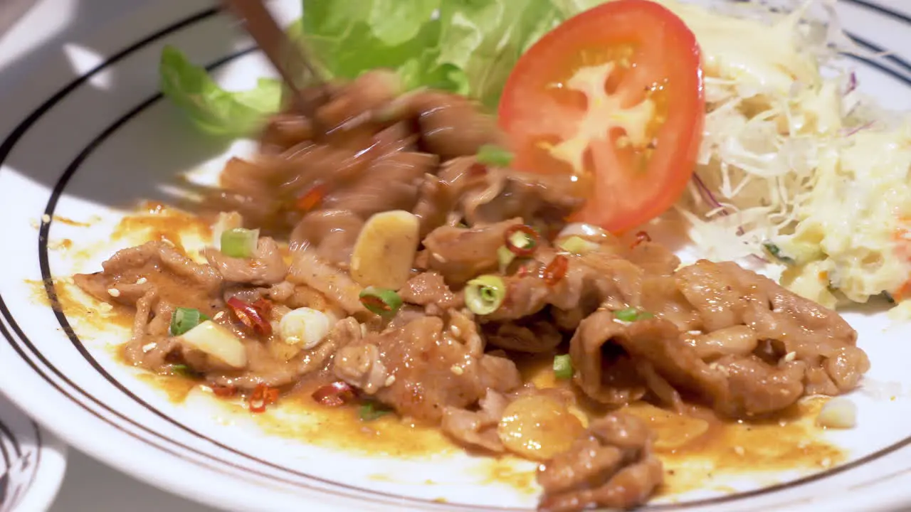 Mixing a plateful of spicy stir-fried meat with vegetable salad of sliced tomato lettuce and cabbage on the sides