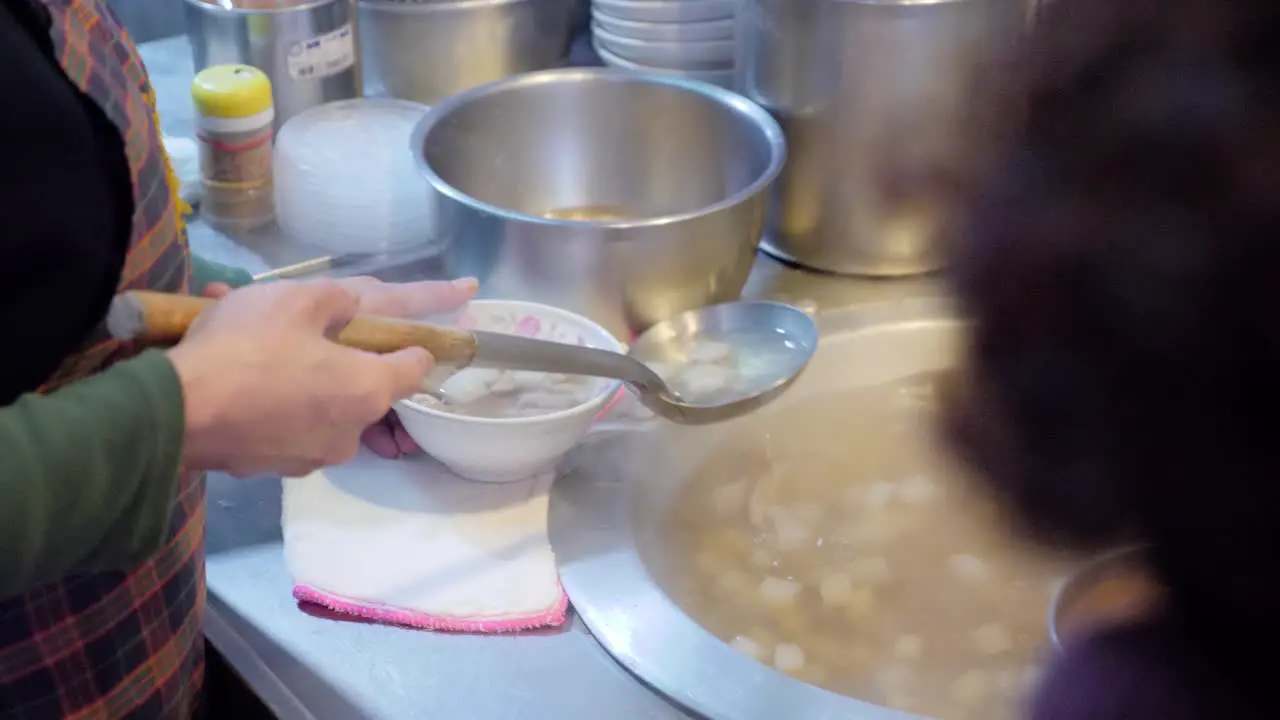 Slow motion shot of woman pouring soup in bowl at street market in Taiwan