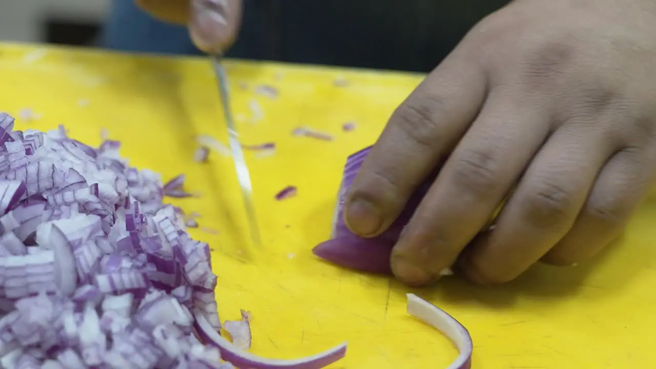 Close-up of hands chopping red onion on a yellow cutting board kitchen setting