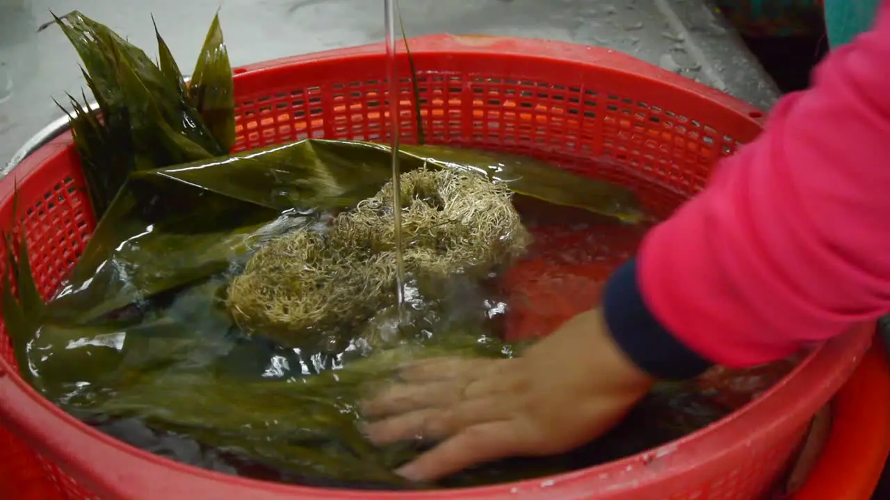 Leaves for wrapping Asian rice triangles being washed clean with water in red basket during food prep