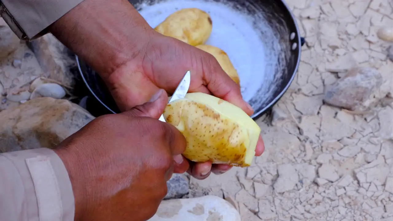 Close up of a mans hands peeling potatoes with a pocket knife in natural outdoors environment preparing lunch at camp during a hike