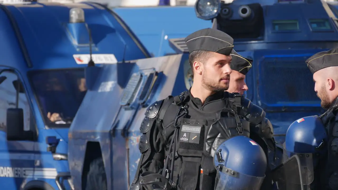 Police officers in full riot gear talk in front of blue police tanks in the middle of the street before a demonstration in Marseille south of France