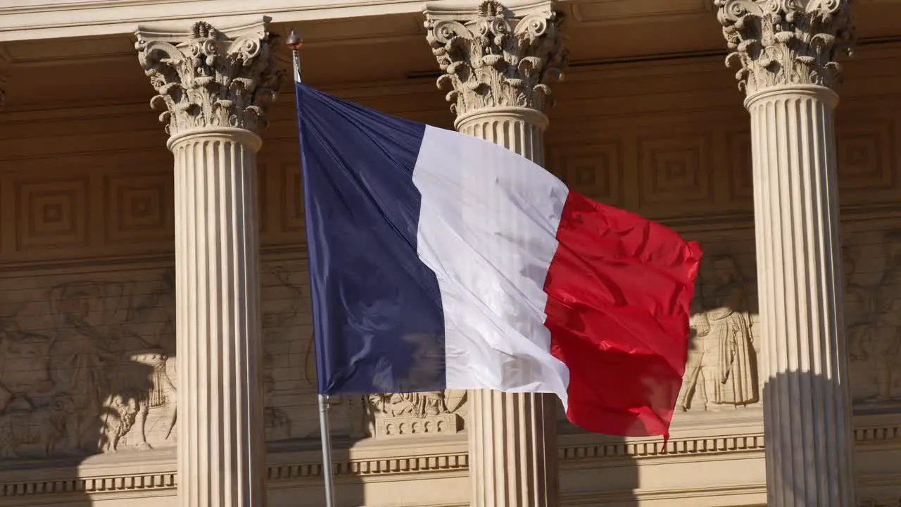 French flag moving in the wind in front of a building inspired by antique Greece columns with its shadow on a wall