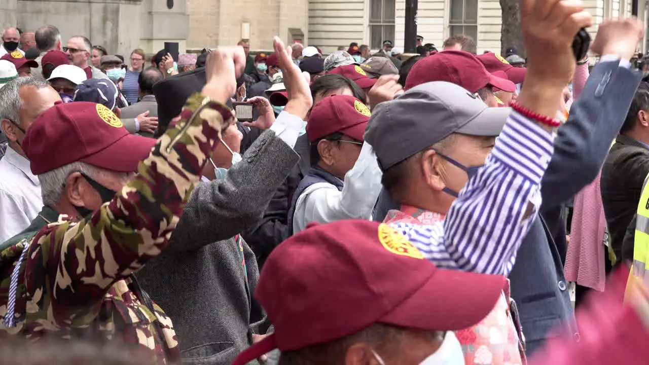 Eldery Ghurka veterans in maroon baseball caps cheer and raise their fists in resistance protest opposite Downing Street calling for full military pensions for all Ghurka veterans